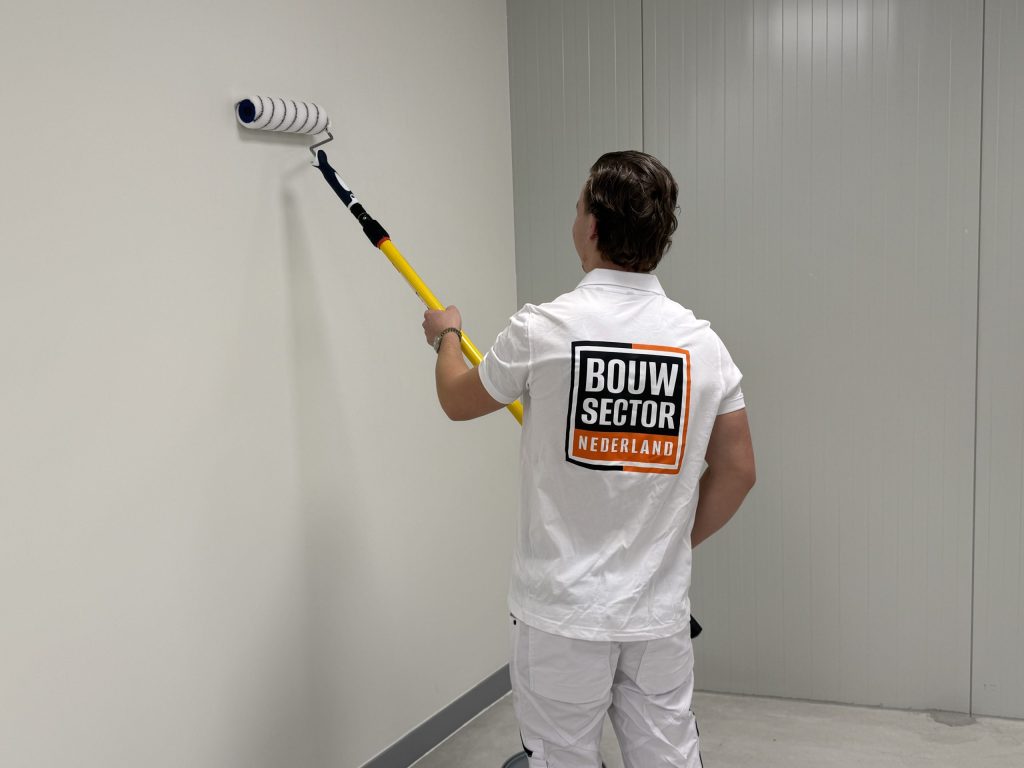 Schilder van Bouwsector Nederland rolt een kale witte wand in een lege kamer