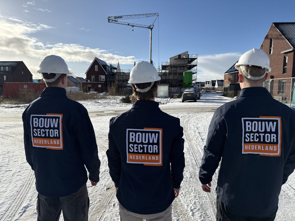 Drie vakmensen van Bouwsector Nederland met witte helm op een nieuwbouwlocatie in de sneeuw
